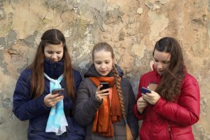 Internet and social networks replace live communication. Three girls together chat using their smartphones outdoor - horizontal